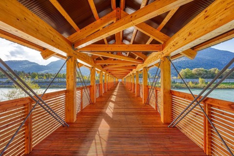 Perspective of a wooden bridge, framed by mountains and river, with modern construction, Inn
