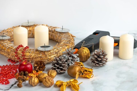 Craft scene with Advent wreath, white candles, decoration material and a glue gun on a marble
