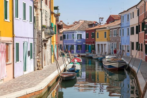 Colourful houses along a quiet canal with parked boats on the island of Burano, Venice, Italy,