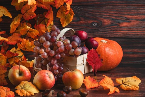 A basket of grapes and plums next to a pumpkin, apples, chestnuts and autumn leaves