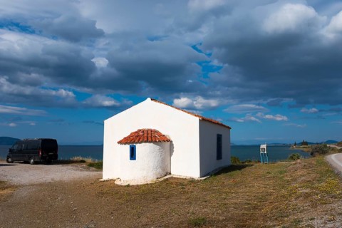 White building with a red roof by the sea, surrounded by a cloudy sky and peaceful countryside. A