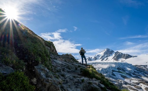 Mountaineer in front of high alpine mountain landscape with sun star, summit of Aiguille de