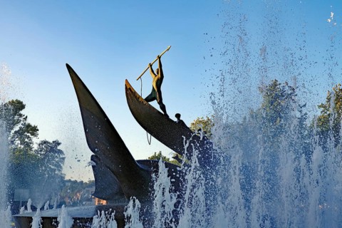 A dynamic statue surrounded by spraying water fountains at sunrise, memorial to the whalers of