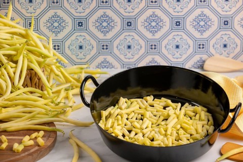 A cooking pot full of sliced beans on a kitchen worktop, whole runner beans in the background