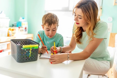 Happy and tender scene of a mother and school boy coloring at home together