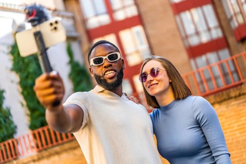 Smiling multiracial cool modern couple vlogging through mobile phone in the city street