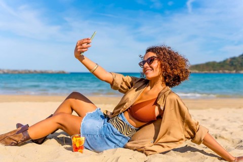 Sensual arab modern woman wearing bikini and denim shorts taking selfie sunbathing on the beach