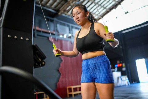 Low angle view three quarter length photo of an asian woman training using lat machine to pull