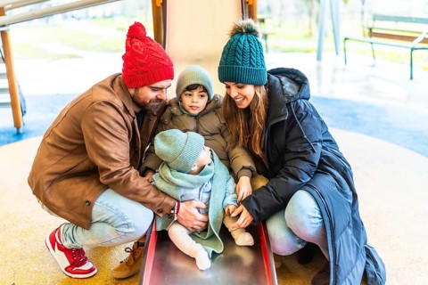 Parents assisting their children as they joyfully slide down a playground slide, embracing the fun