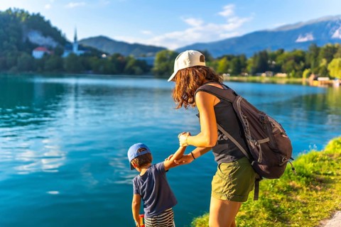Mother and son holding hands, enjoying summer vacation by the turquoise water of lake bled, with