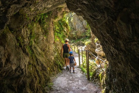 Mother and son walking through a natural rock tunnel, enjoying the stunning views of tolmin gorge