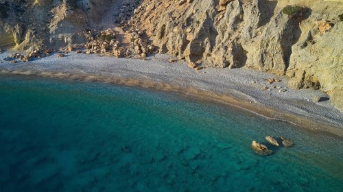 Quiet stretch of beach with rocky coastline and crystal clear water in turquoise blue colour, drone