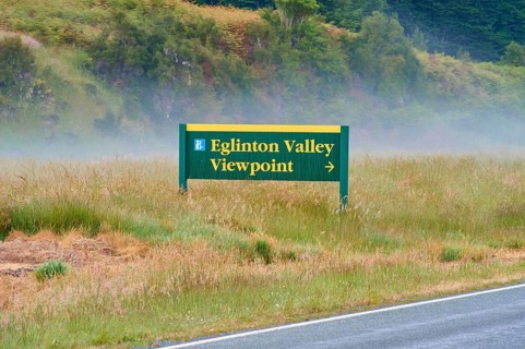Sign showing the way to Eglinton Valley viewpoint, surrounded by misty pasture, summer, Milford