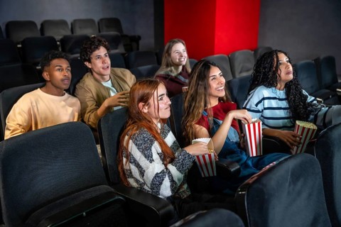 Group of diverse friends enjoying a film at the movie theater, eating popcorn and having fun