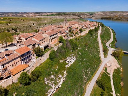 A village on a river with a raised road and green surroundings as well as densely built-up houses,