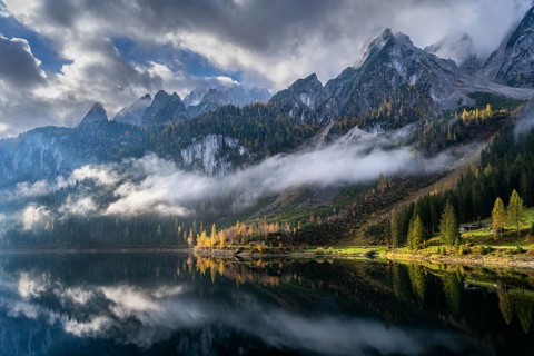 The Vordere Gosausee in autumn with a view of the Gosaukamm. Cloudy sky with sun. Trees in autumn