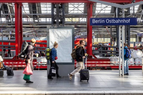 Construction site at Ostbahnhof station with station sign, travellers on the platform. Berlin,