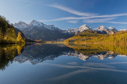 Lake Almsee in autumn with a forest and mountains reflected in the lake. A slowly dissipating fog