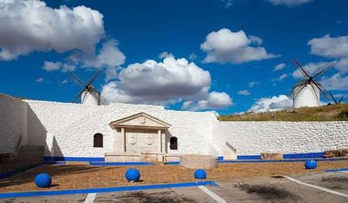 Two windmills and a stone wall against a blue sky full of clouds, Fuente del Caño, open-air museum,