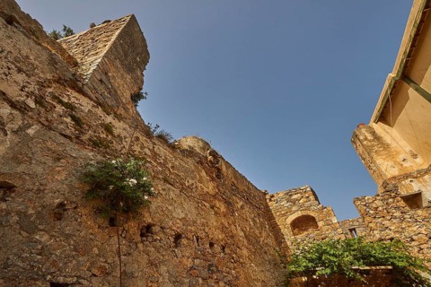 An old stone wall with vegetation and ruins under a bright blue sky, Venetian Sea Fortress, Leper