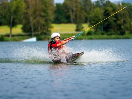 Boy or girl, sitting on wakeboard, cheerful, red life jacket, water skiing and summer holiday in