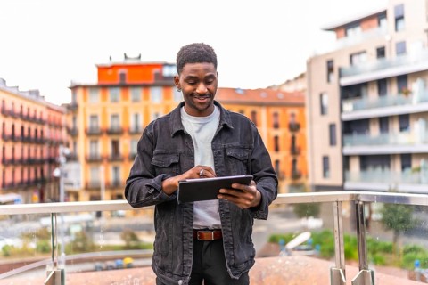 Frontal three quarter length photo of a happy young african man using digital tablet standing in a