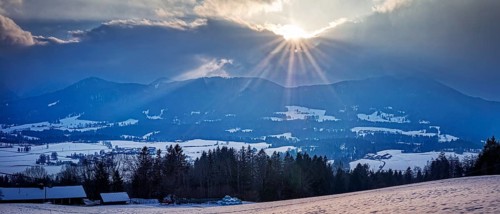 Winter landscape with mountains in the background and sunbeams through the clouds, Fischbachau