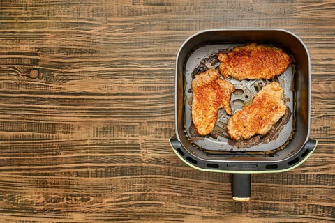 Three pork chops are sizzling in an air fryer basket, each one showcasing a crispy golden crust