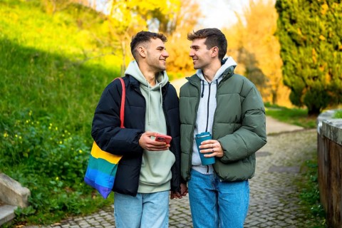 Happy caucasian gay couple holding hands and walking in a park, enjoying a relaxing moment together
