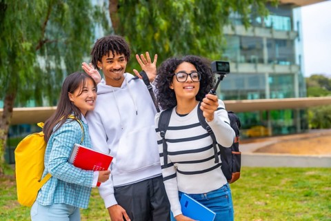Three multi-ethnic students waving while recording a video with a wearable camera standing outside