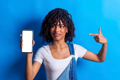 Studio portrait of a young woman holding a smartphone with blank white screen and pointing at it
