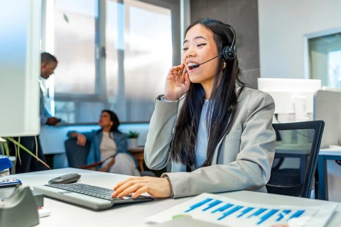 Young asian manager talking on headset and working on computer in a bright coworking office with