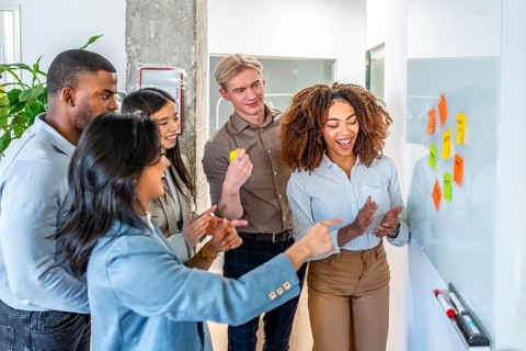 Diverse colleagues brainstorming and planning using colorful sticky notes on a whiteboard,