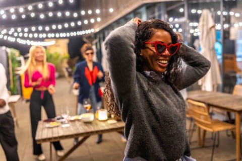 Funny latin woman with heart-shaped sunglasses and casual winter clothes dancing next to friends at