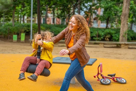 Happy scene of a caucasian adult mother playing with a girl swinging in a park