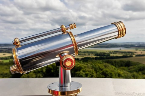 Metallic telescope points into the distance over a vast landscape under a cloudy sky, Rügen,