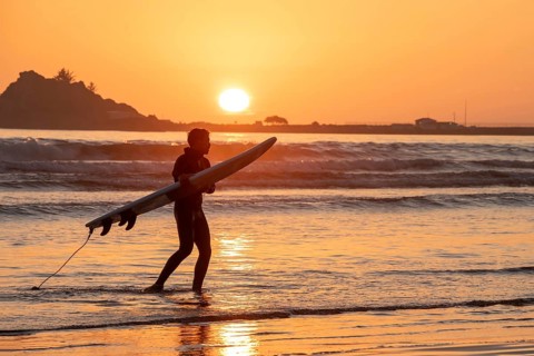 Crescent City, California - A surfer takes his board out of the water as the sun sets over the