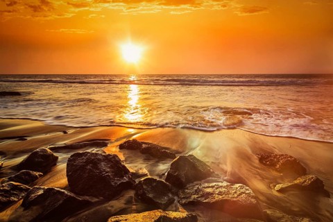 Tropical beach vacation background, waves and rocks on beach on sunset with beautiful cloudscape.
