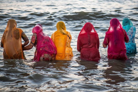 Hindu pilgrims, woman in colourful saris, take a holy dip in the sea in front of sunrise at Ghat