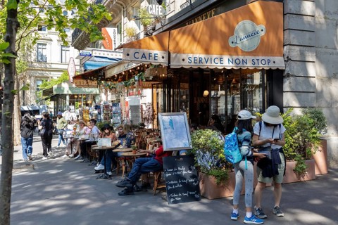 Street café with several guests outside under an orange awning on a sunny day, Paris