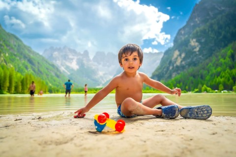Young boy playing with toy cars on the sandy shore of lago di landro, surrounded by the stunning