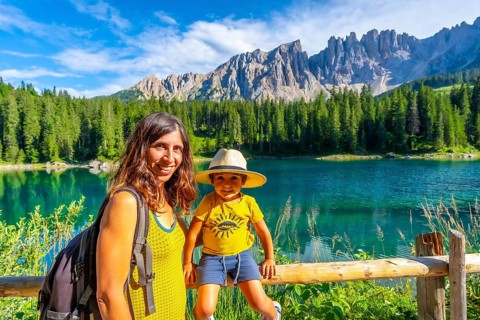 Mother and son enjoying the stunning scenery of lake carezza with the latemar mountain range in the