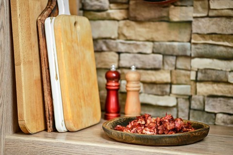A rustic kitchen features a plate of chopped bacon next to wooden cutting boards. Two shakers, one