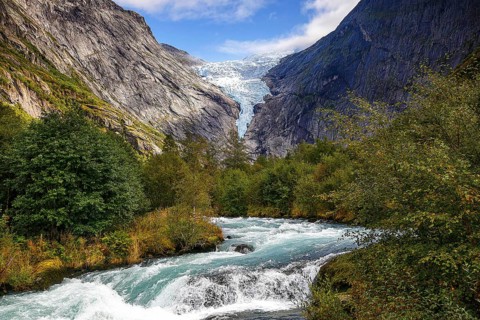 River flanked by mountains flows through a green valley with a view of the shimmering