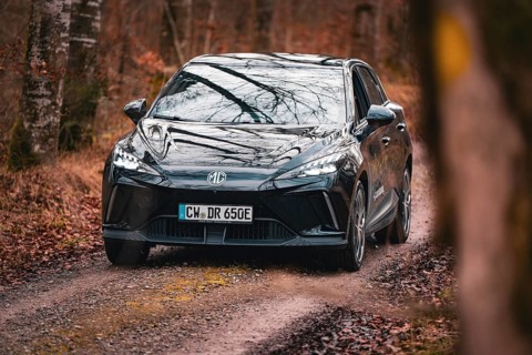 Black limousine drives along a narrow forest path through autumnal surroundings, e-car sharing