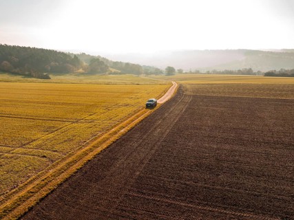 Landscape shot of a car on a path between golden and brown fields in sunlight, electric car VW ID5,