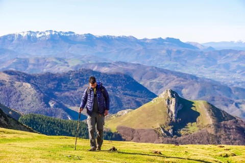Male hiker walking on a grassy mountain slope with scenic views of the pyrenees mountains in the