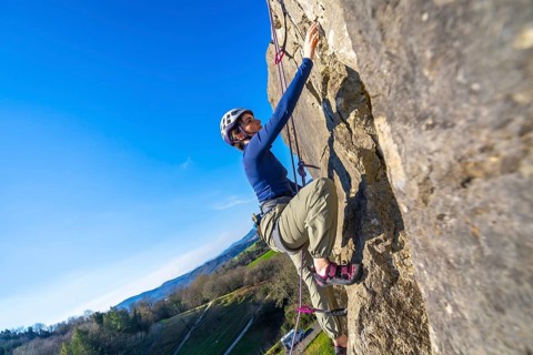 Female climber ascending challenging rock face on a sunny day, enjoying the thrill of outdoor