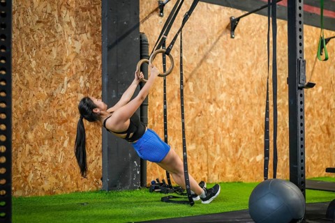Full length side view of an asian strong woman exercising biceps using gym rings in a modern gym