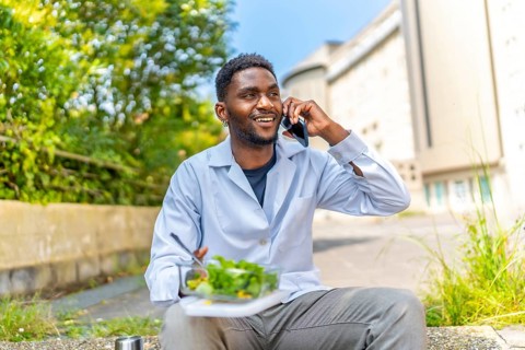 African doctor talking to the phone during lunch break sitting outside the hospital